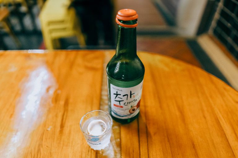 Korean Alcohol Guide: Soju, Makgeolli, Sake Comparisons & Drinking Culture 6 Korean soju bottle with shot glass on a wooden table in a cozy setting.